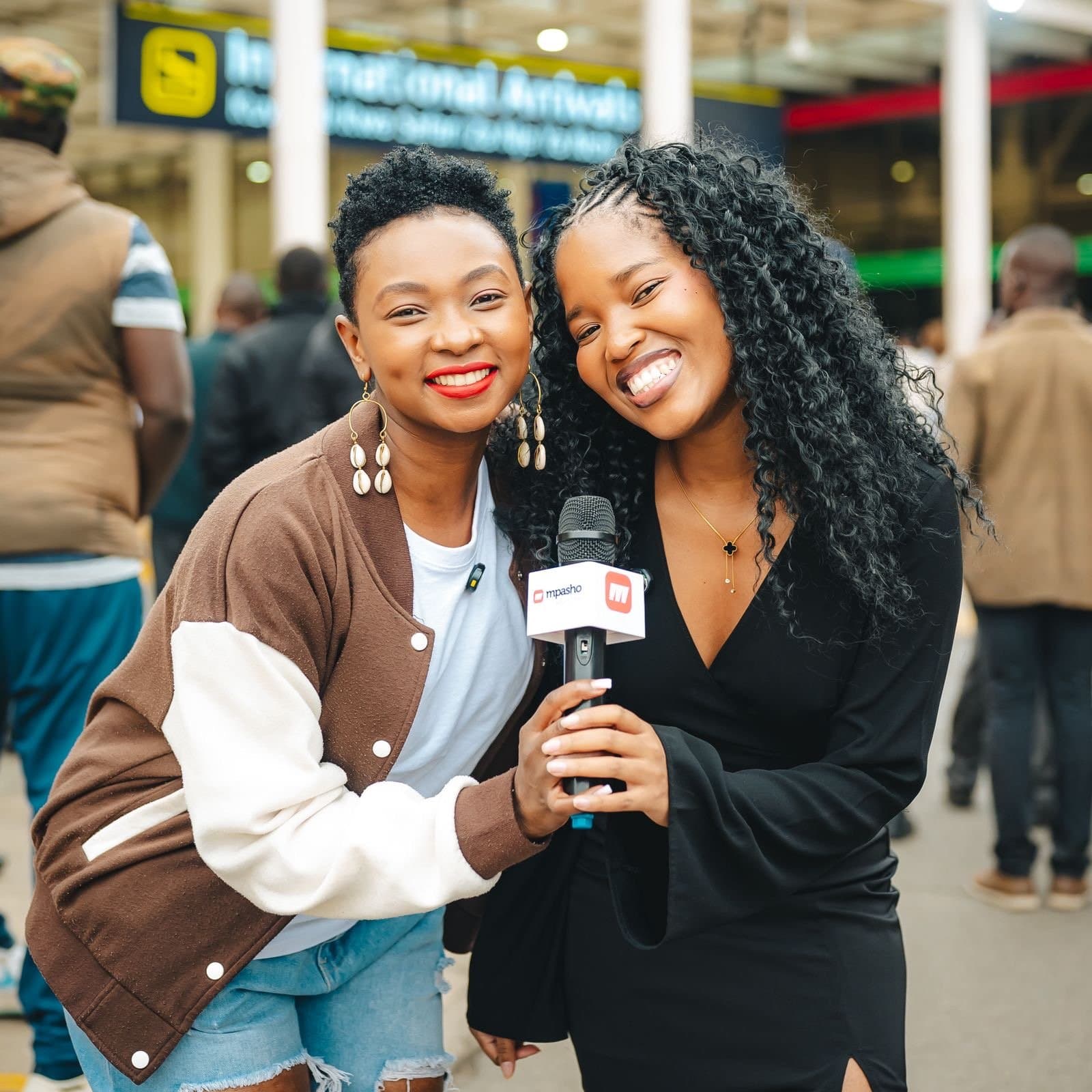 Primrose and a fellow reporter with an Mpasho microphone outside International Arrivals